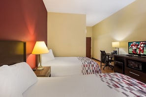A hotel room with two beds, a desk, a television, and a lamp.