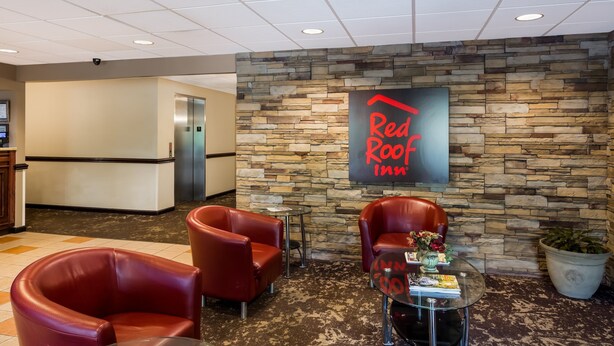 Un hall d’entrée de Red Roof Inn avec des murs en pierre, des fauteuils en cuir, un comptoir d’accueil et une table basse avec des magazines.