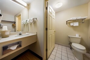 Een badkamer met een toilet, wastafel, spiegel, handdoekrek en een plank met handdoeken.