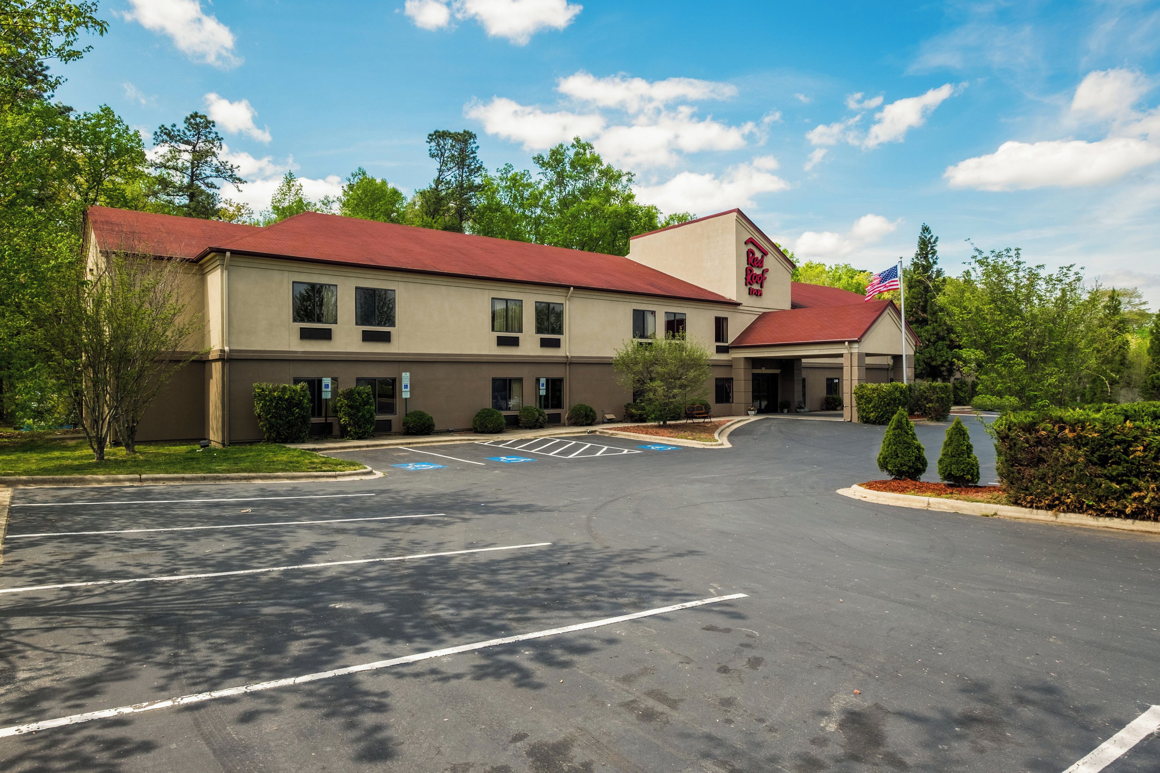 A hotel with a red roof, a parking lot with marked handicapped spaces, and a flagpole with an American flag.