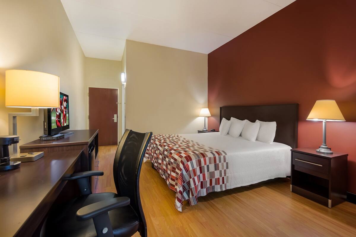 Een hotelkamer met een bed, nachtkastjes, een bureau met stoel, een televisie en een lamp.
