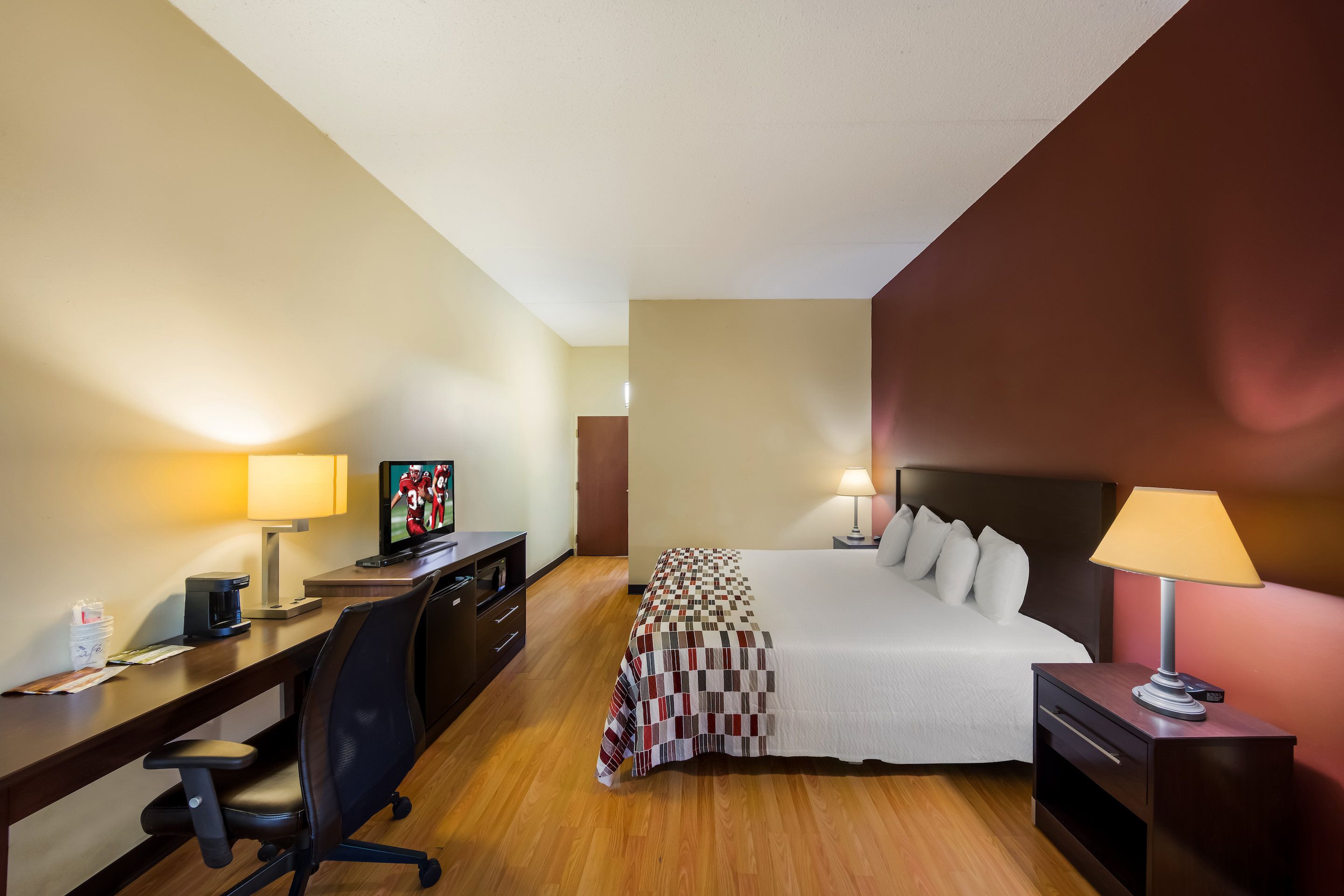 A hotel room with a bed, desk, chair, television, and bedside lamps.