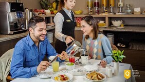 A breakfast setting with a coffee machine, a server pouring a drink, and guests seated at a table with plates of food and a coffee cup. - Hotel Casa Spark Santiago (Santiago)