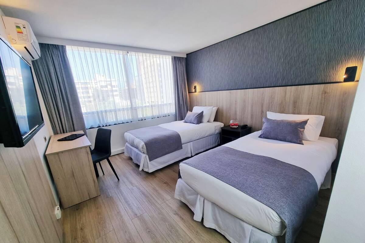 Habitación de hotel con dos camas, un escritorio, una silla, un televisor y una ventana con cortinas.