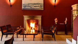 A cozy lounge area with a fireplace, comfortable seating, and a framed cityscape painting. - Casa Melo Alvim by Unlock Hotels (Viana do Castelo)
