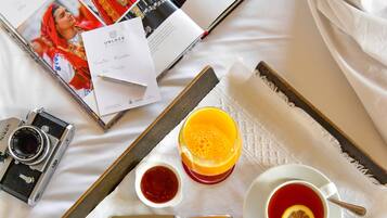 A neatly arranged breakfast tray with a camera, a magazine, and a book on a bed.