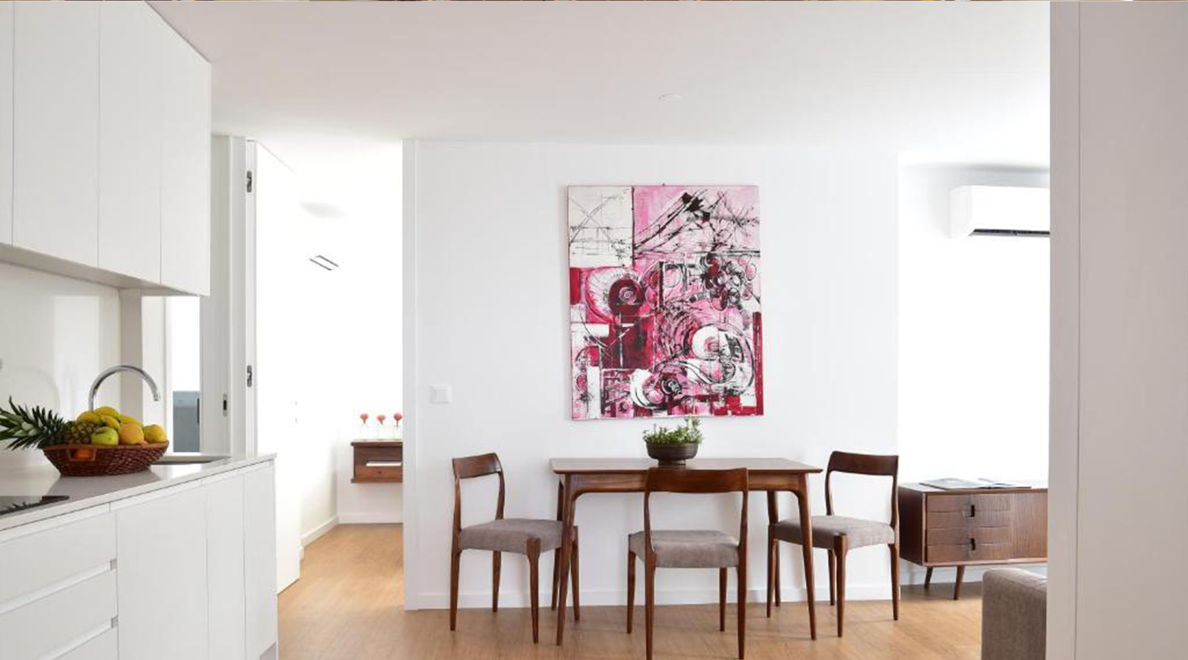 Una cocina moderna con armarios blancos, una mesa de comedor con cuatro sillas y un cuadro abstracto grande en la pared.