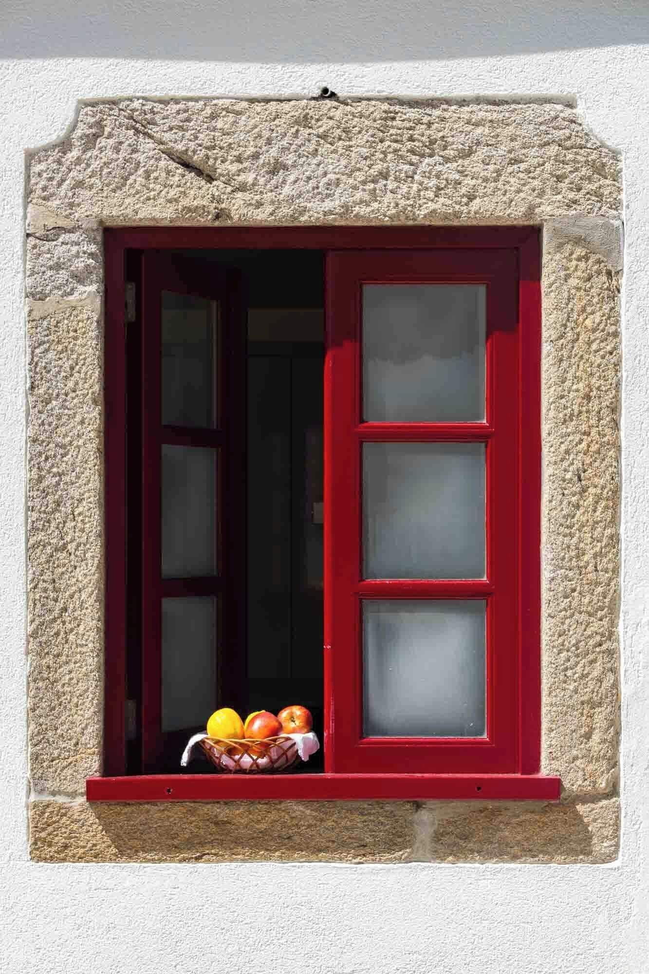 Una ventana con marco rojo y pared de piedra.