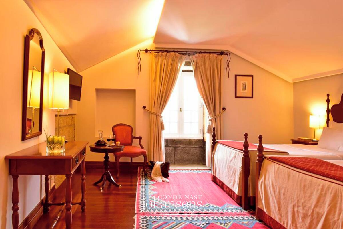 A hotel room with a bed, a chair, a table, and a mirror.