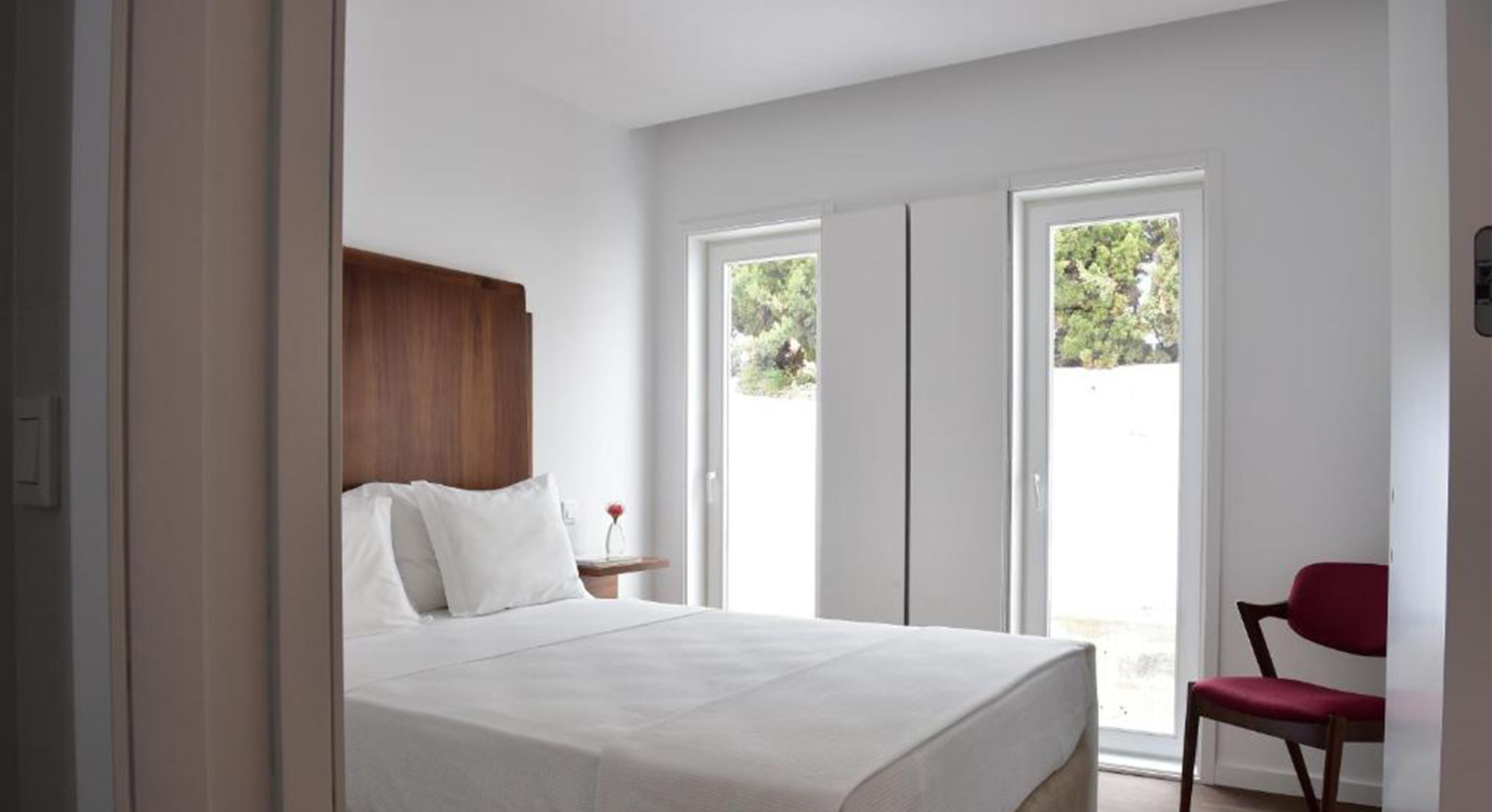 A bedroom with a bed, a wooden headboard, a nightstand, a red chair, and a sliding glass door leading to an outdoor area.