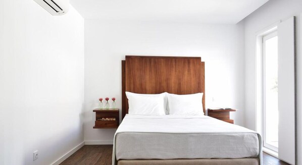 A hotel room with a large bed, wooden headboard, white bedding, a nightstand with a vase of flowers, and a window providing natural light. - Casa Melo Alvim by Unlock Hotels (Viana do Castelo)