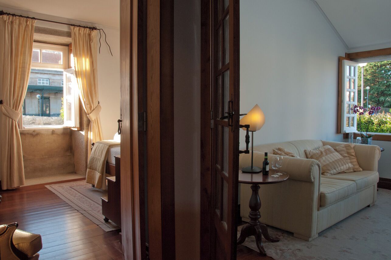 A cozy room with a sofa, a small table with a lamp, and a window with curtains.