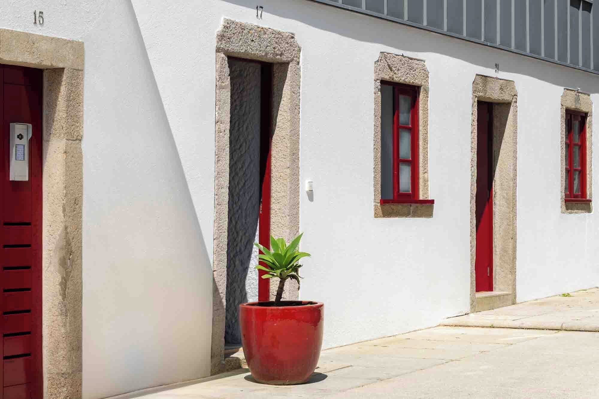 A building with white walls and red doors, featuring a potted plant in the foreground.