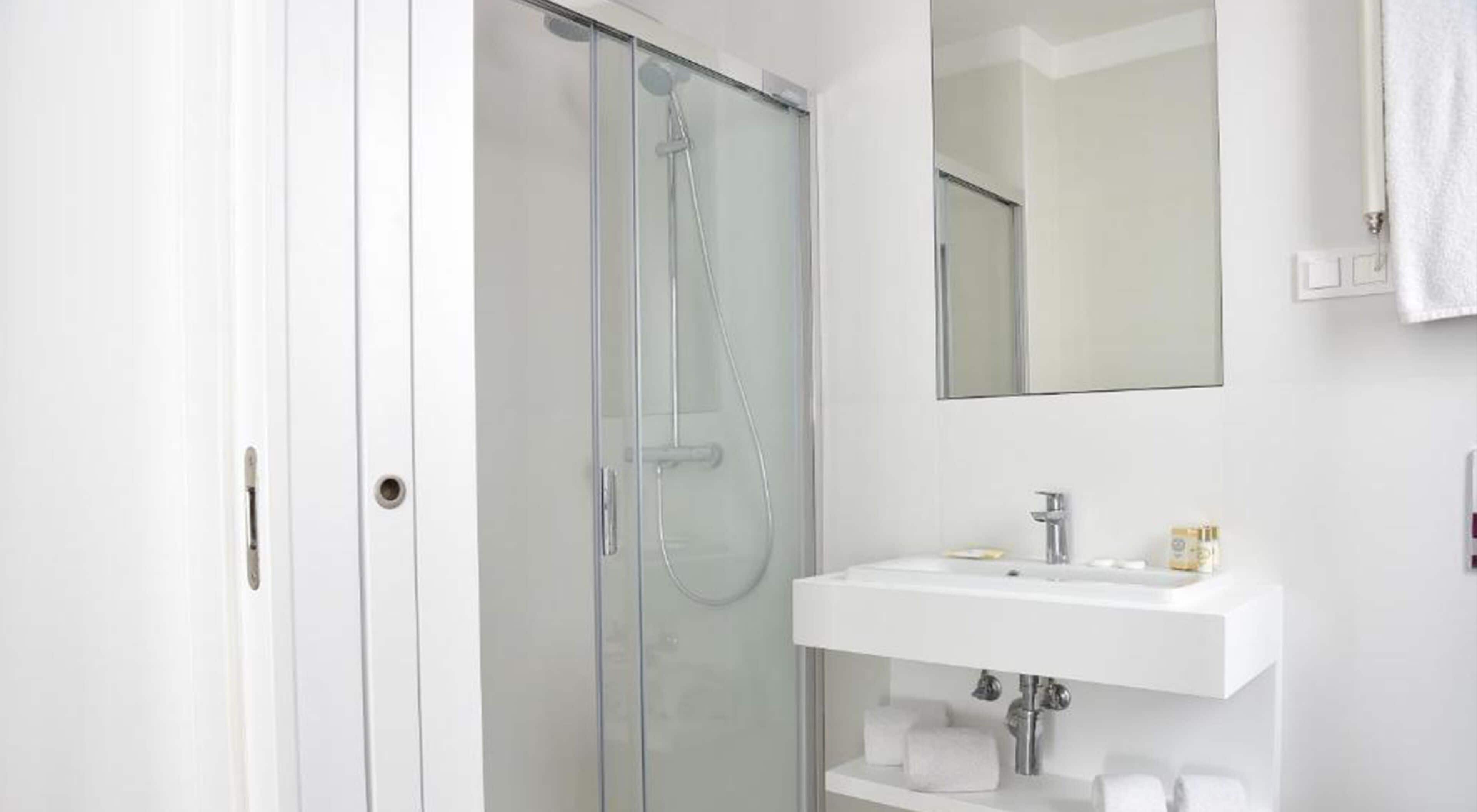 Une salle de bain moderne avec une douche à l’italienne en verre, un lavabo blanc et un miroir au-dessus.