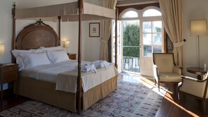 A four-poster bed with a wooden headboard, a bedside table, a chair, and a small table with a lamp. - Casa Melo Alvim by Unlock Hotels (Viana do Castelo)