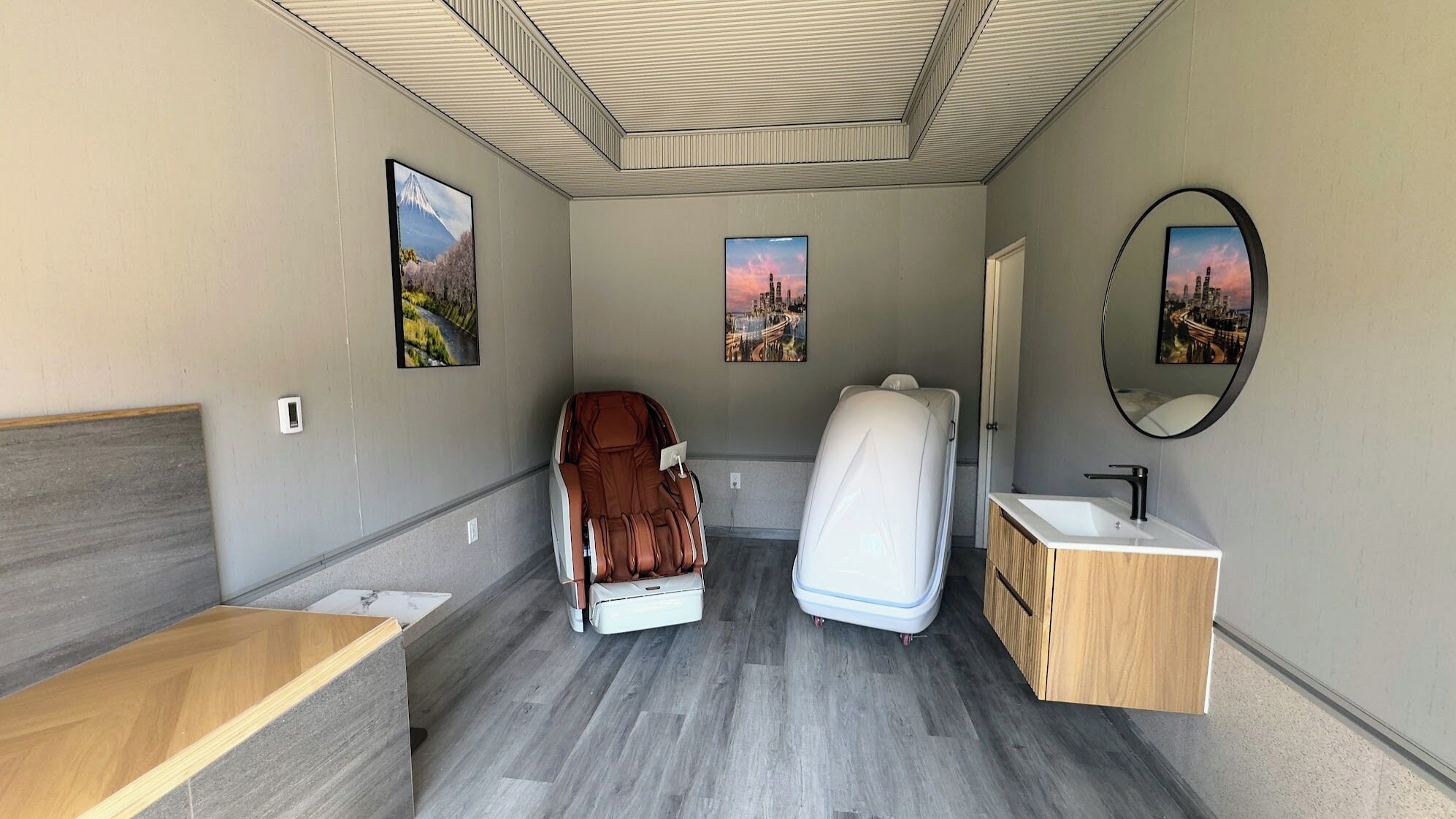A modern bathroom with a wooden bench, a white bathtub, a wooden vanity with a sink, and two framed pictures on the walls.