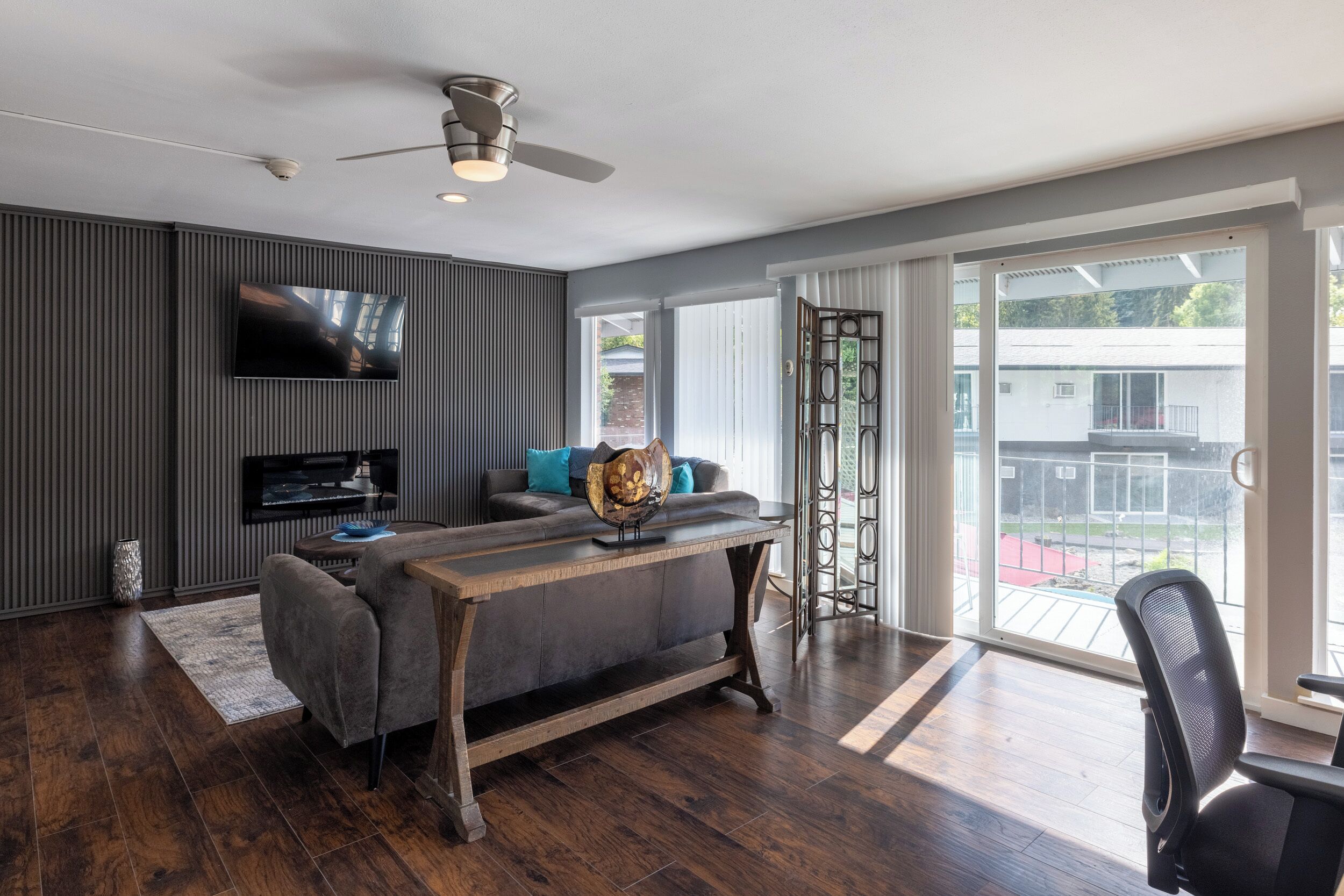 A modern living room with a flat-screen TV, a sofa, a coffee table, and a large window with a view of the outside.