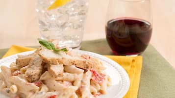 A plate of pasta with chicken and a glass of red wine.