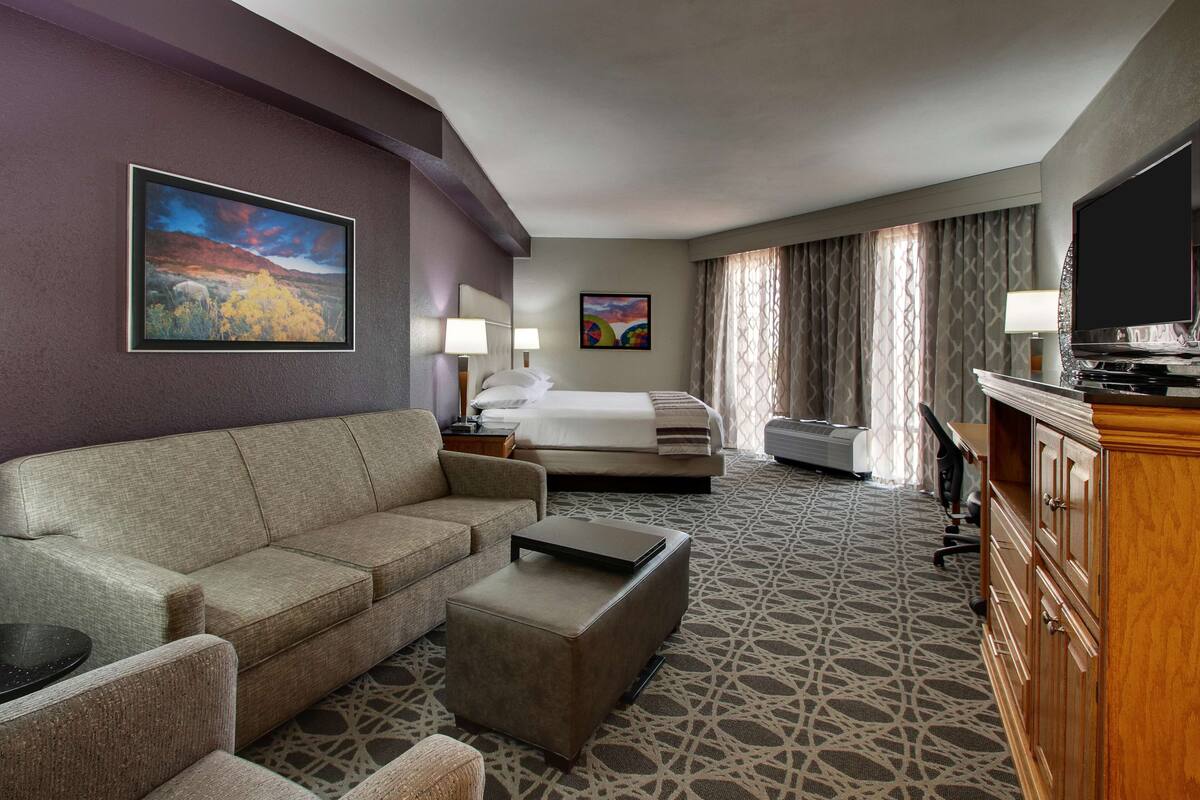 Ein Hotelzimmer mit einer Couch, einem kleinen Tisch, einem Bett, einem Fernseher und einem Schrank.