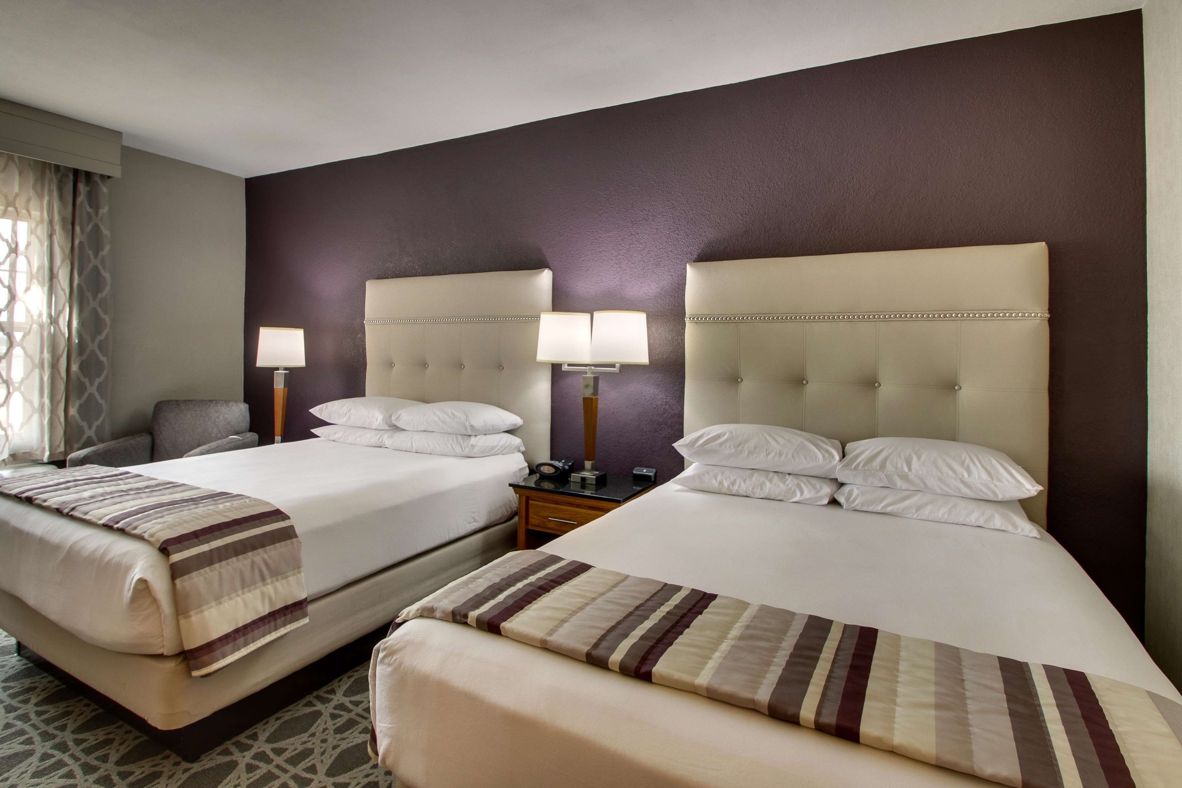 A hotel room with two beds, each with a headboard, bedside tables, lamps, and a striped blanket.