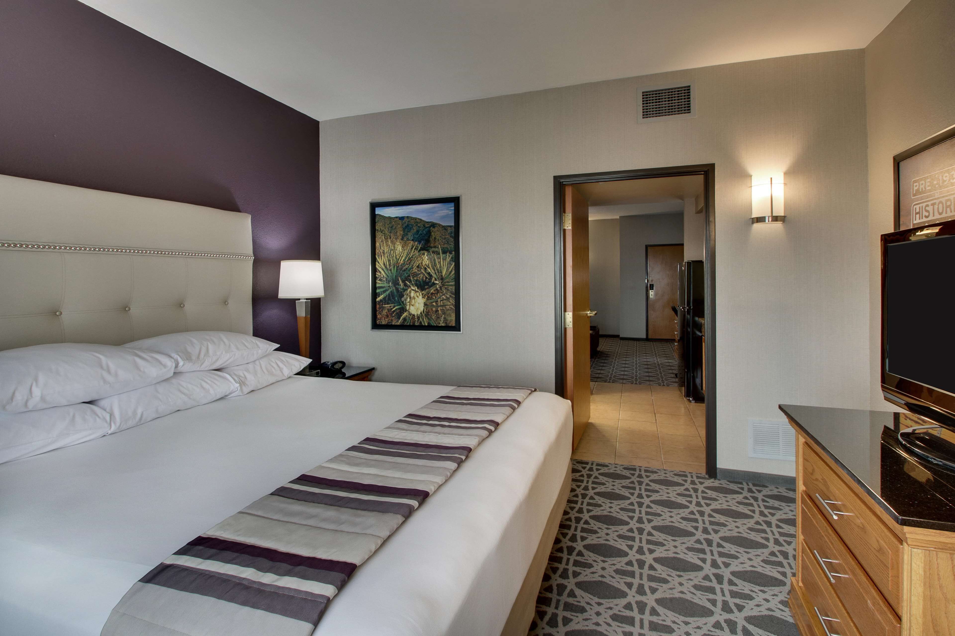 A hotel room with a large bed, a TV, a wooden dresser, and a painting on the wall.