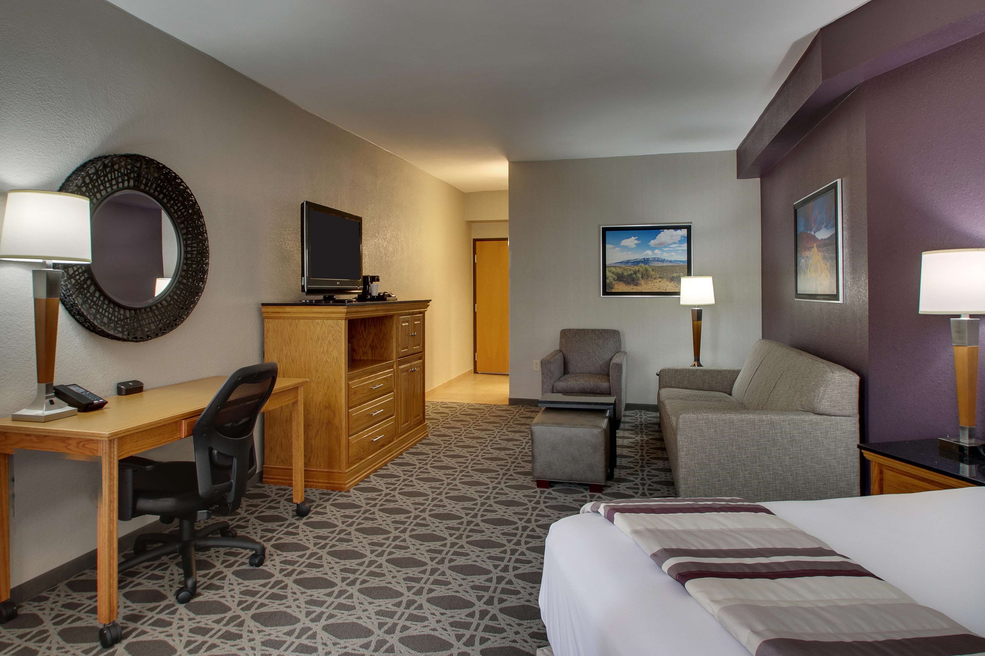 A hotel room with a bed, desk, chair, and a television on a wooden cabinet.