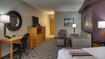 A hotel room with a bed, desk, chair, and a television on a wooden cabinet.