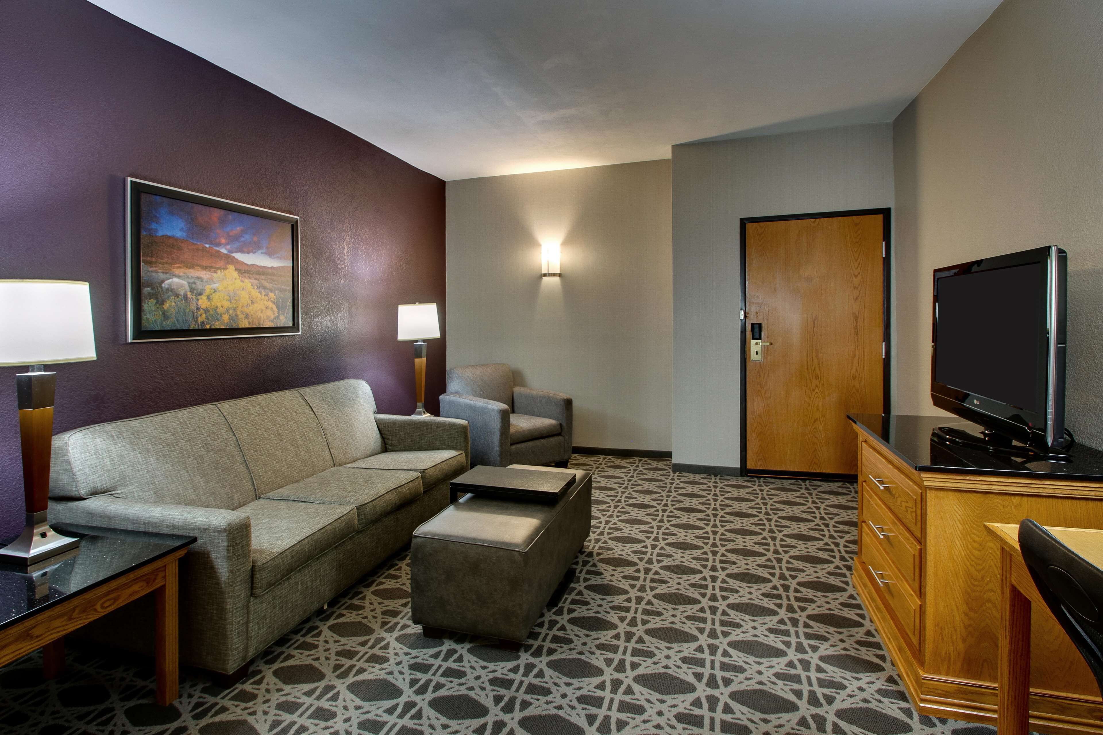 A hotel room with a sofa, armchairs, a TV, a desk, and a patterned carpet.