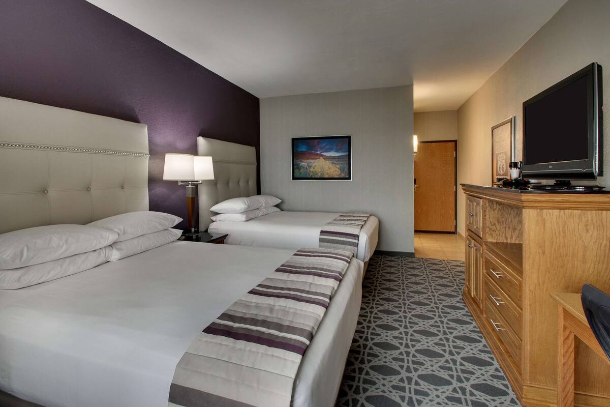 Ein Hotelzimmer mit zwei Betten, einem Fernseher, einer hölzernen Kommode und einem Bild an der Wand.