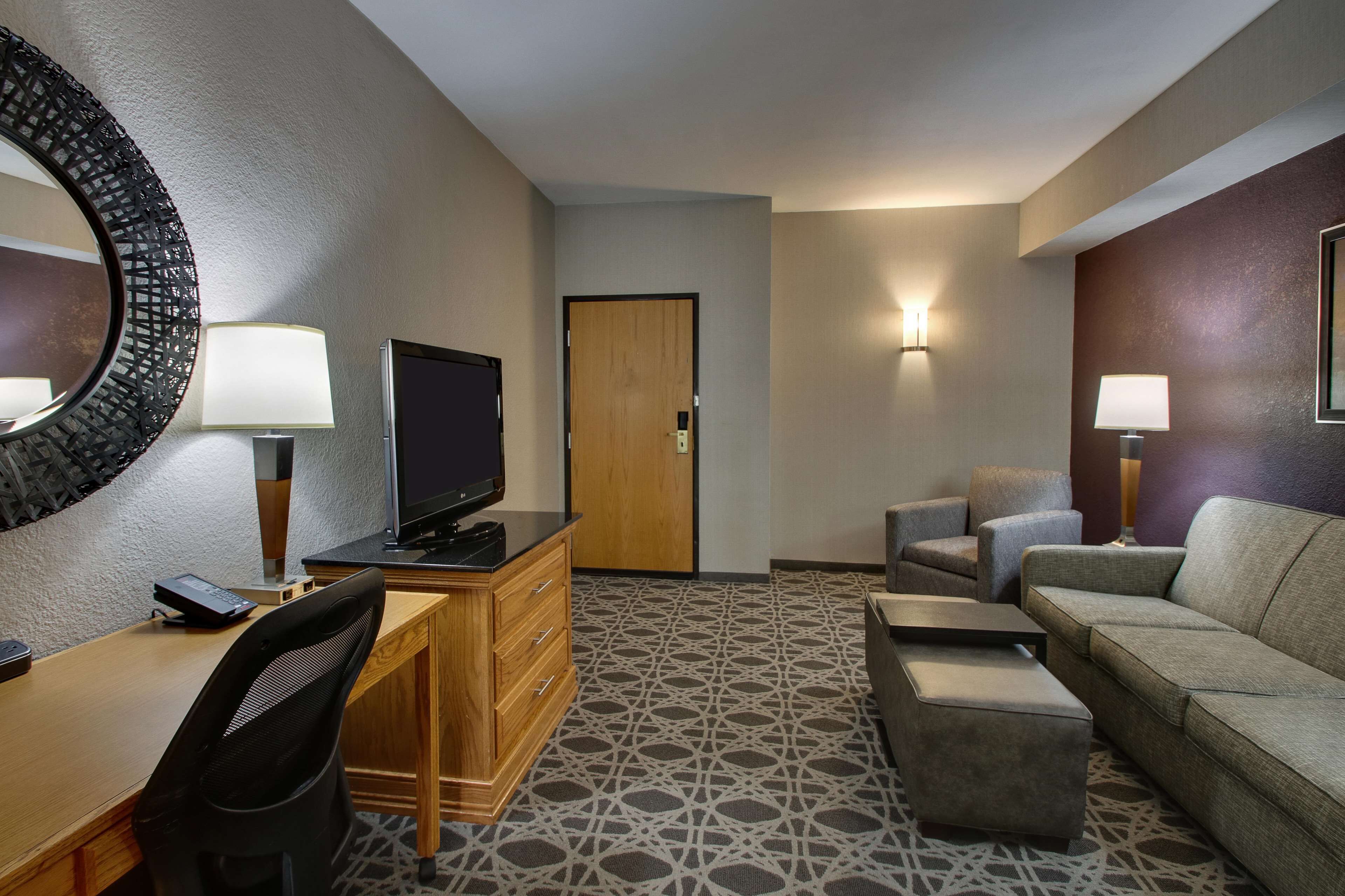 A hotel room with a desk, a television, a sofa, and a patterned carpet.