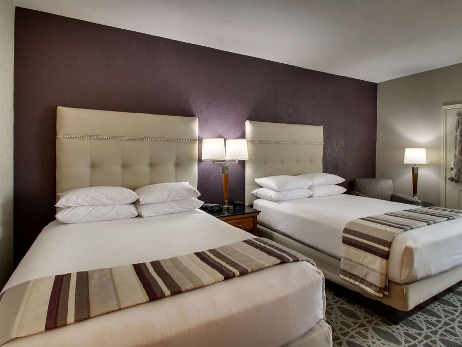 A hotel room with two beds, a headboard, bedside lamps, and a framed picture on the wall.