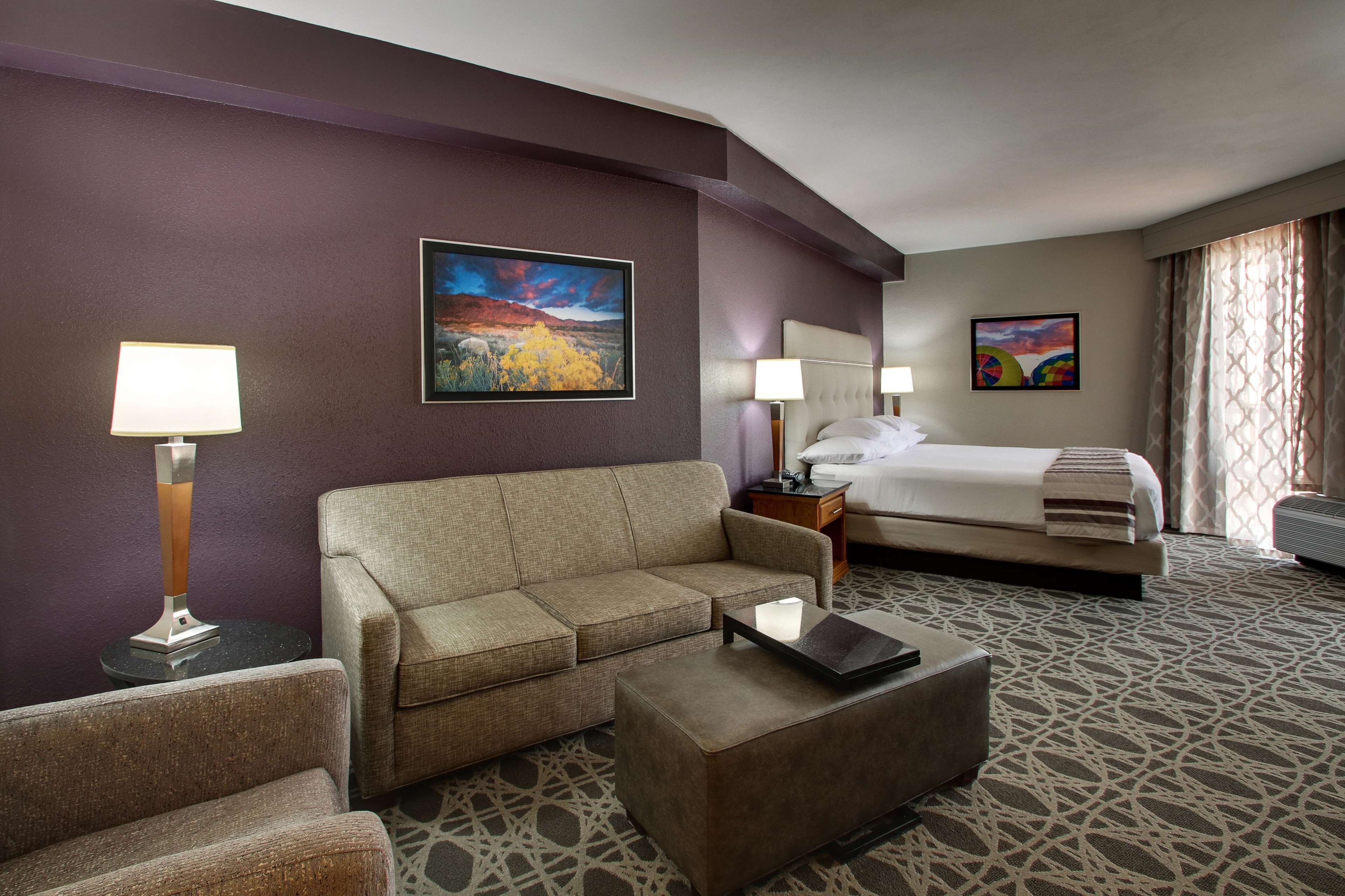 A hotel room with a sofa, a coffee table, a bed, and two paintings on the walls.