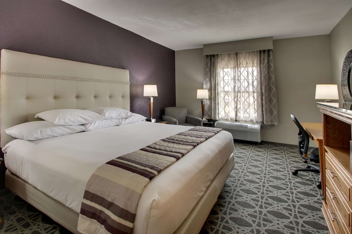 Ein Hotelzimmer mit einem großen Bett, zwei Nachttischen mit Lampen, einem Schreibtisch und einem Sessel.