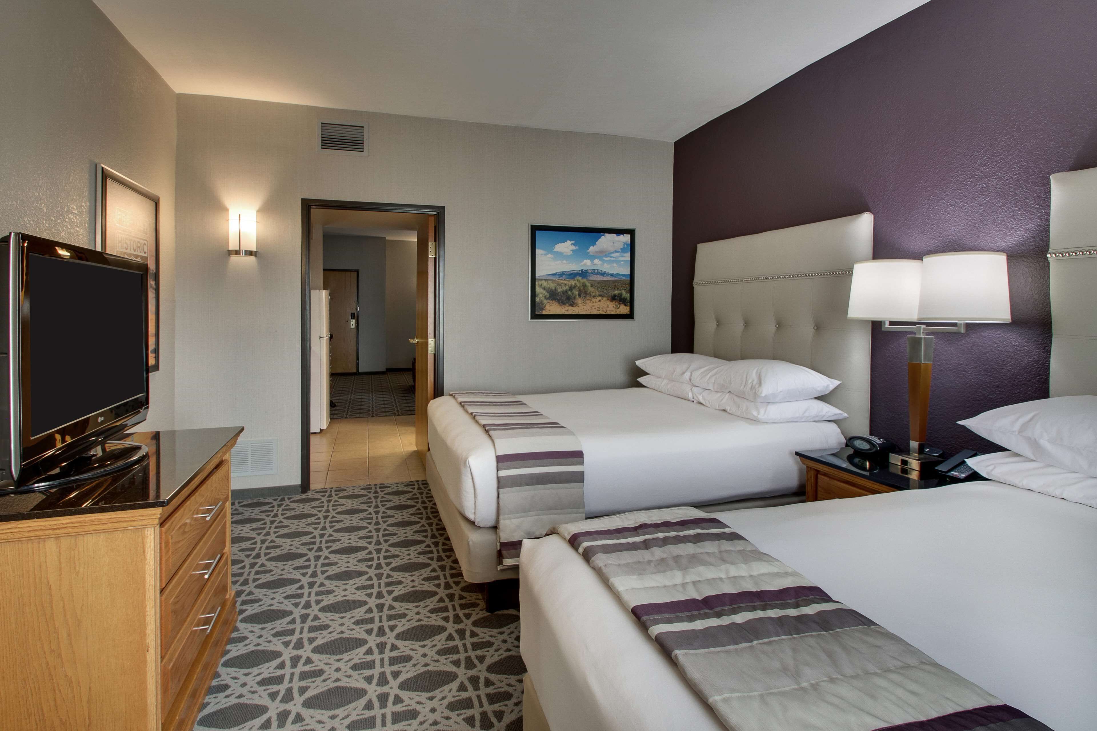 A hotel room with two beds, a TV, a desk, and a lamp.