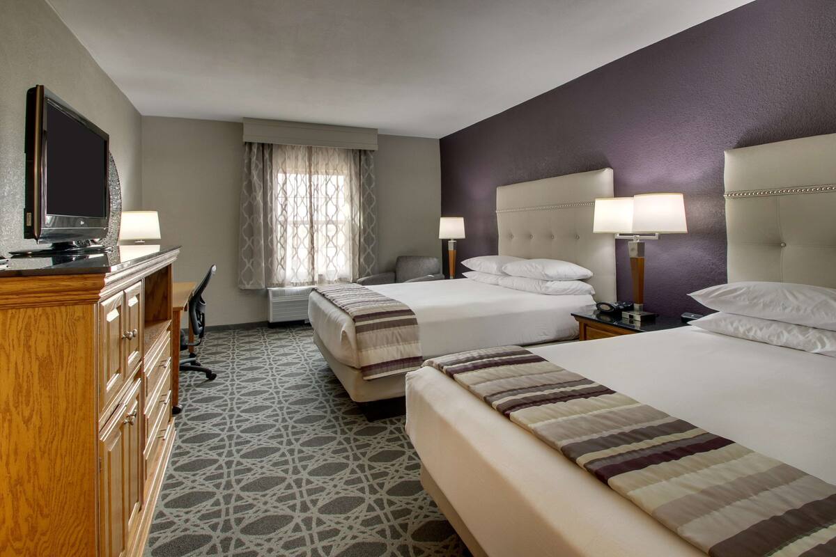 Ein Hotelzimmer mit zwei Betten, einem Fernseher, einem Schreibtisch und einem Sessel.