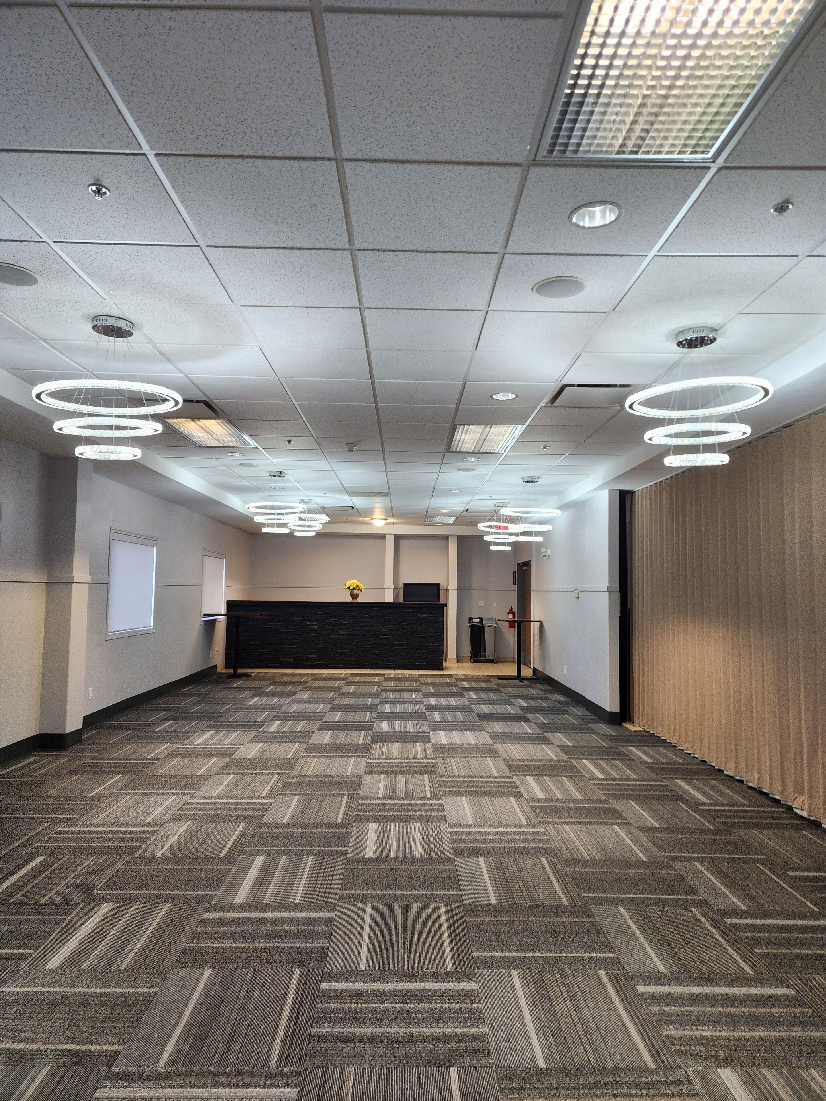 A spacious conference room with a patterned carpet, a reception desk, and multiple ceiling lights.