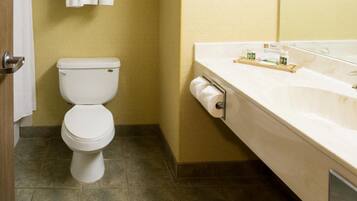 A bathroom with a toilet, a towel rack with folded towels, a sink with a mirror, and a toilet paper holder.