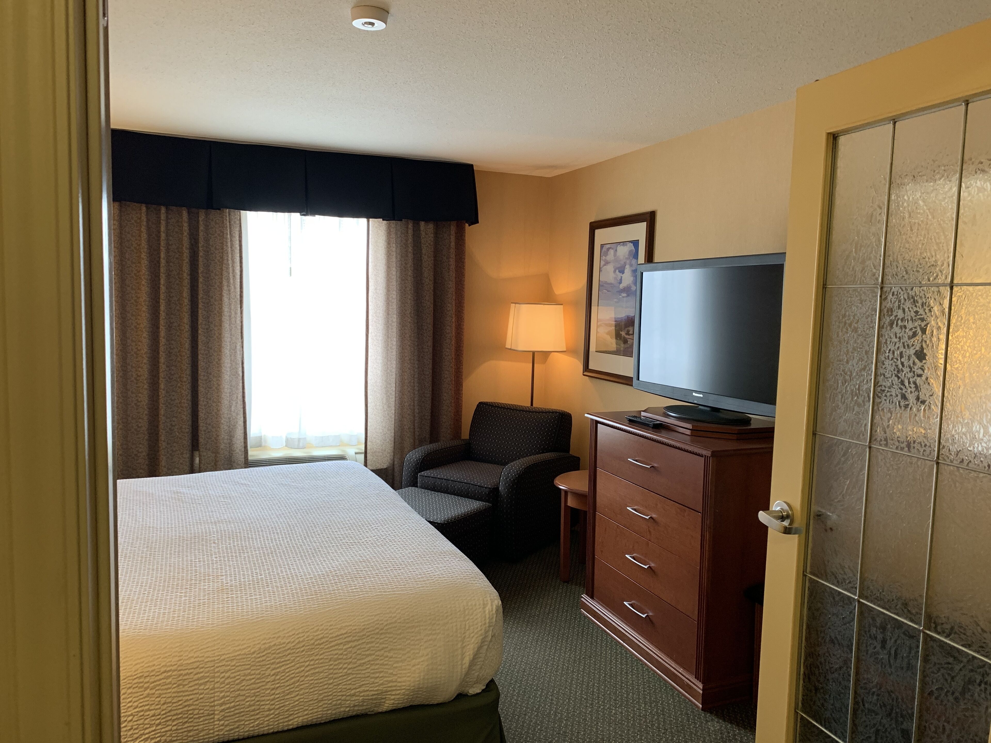 A hotel room with a bed, a television on a wooden dresser, a chair, and a lamp.