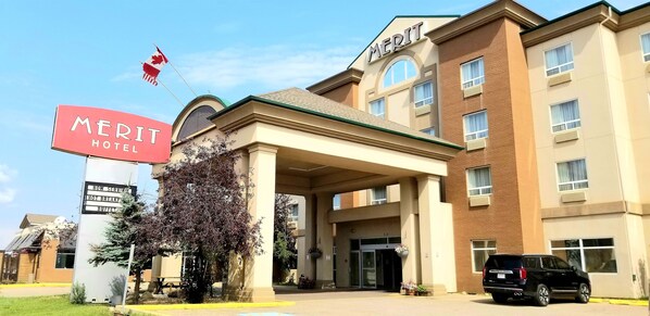 A hotel with a prominent 'MERIT HOTEL' sign, a flag, and a building entrance. - Merit Hotel & Suites (Fort McMurray)