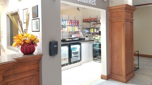 A market entrance with a sign, refrigerated display cases, and shelves stocked with products.