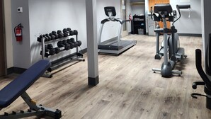A gym with a treadmill, elliptical, dumbbells, and a bench.