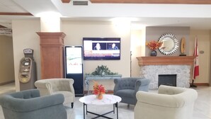 A lobby with four armchairs, a coffee table, a fireplace, a television, and an ATM.