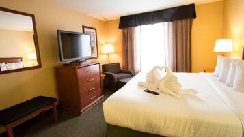Quarto de hotel com uma cama, televisão, escrivaninha com luminária, cadeira e um banco.