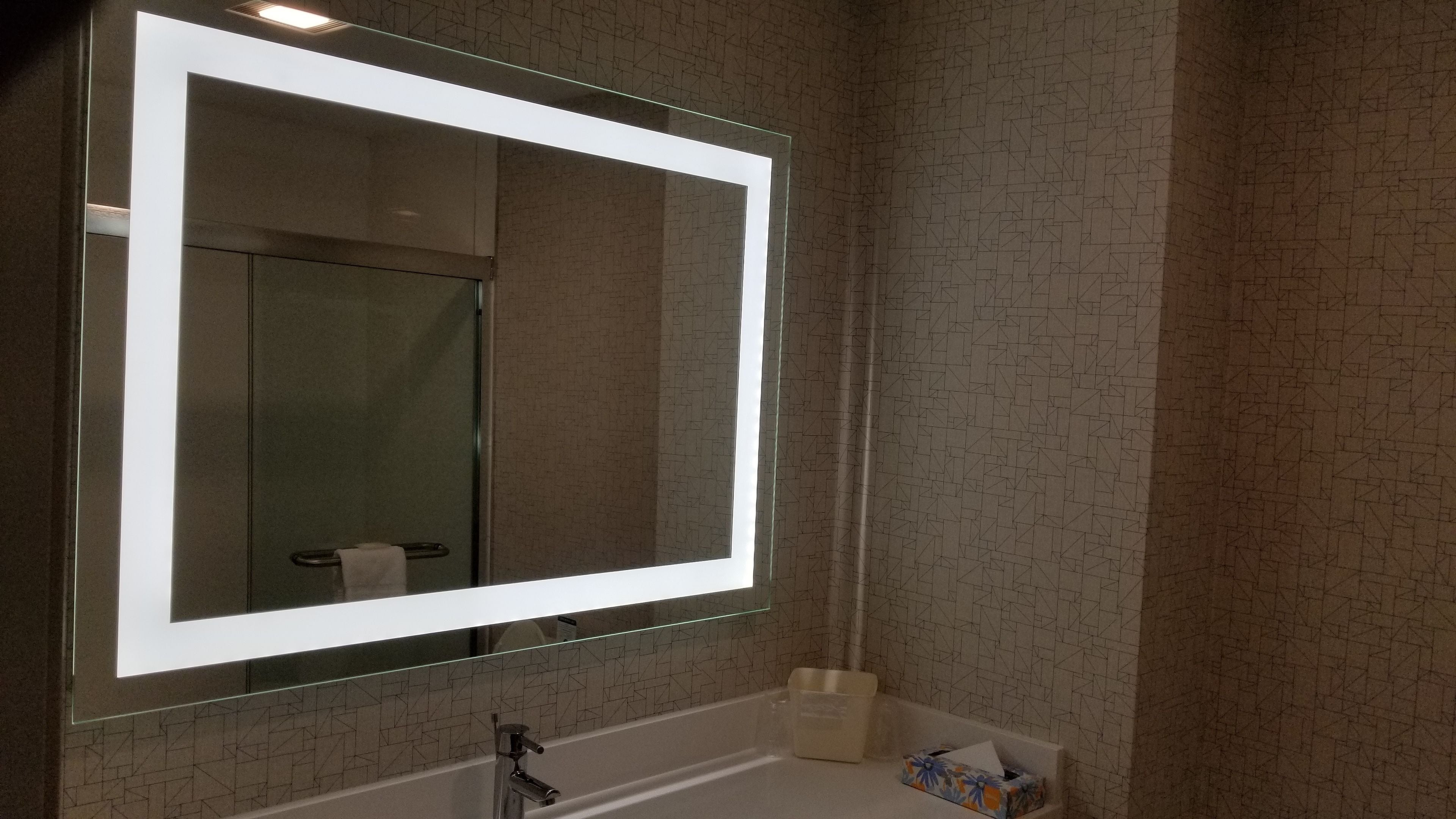 A bathroom with a large mirror, a sink, and a towel rack.