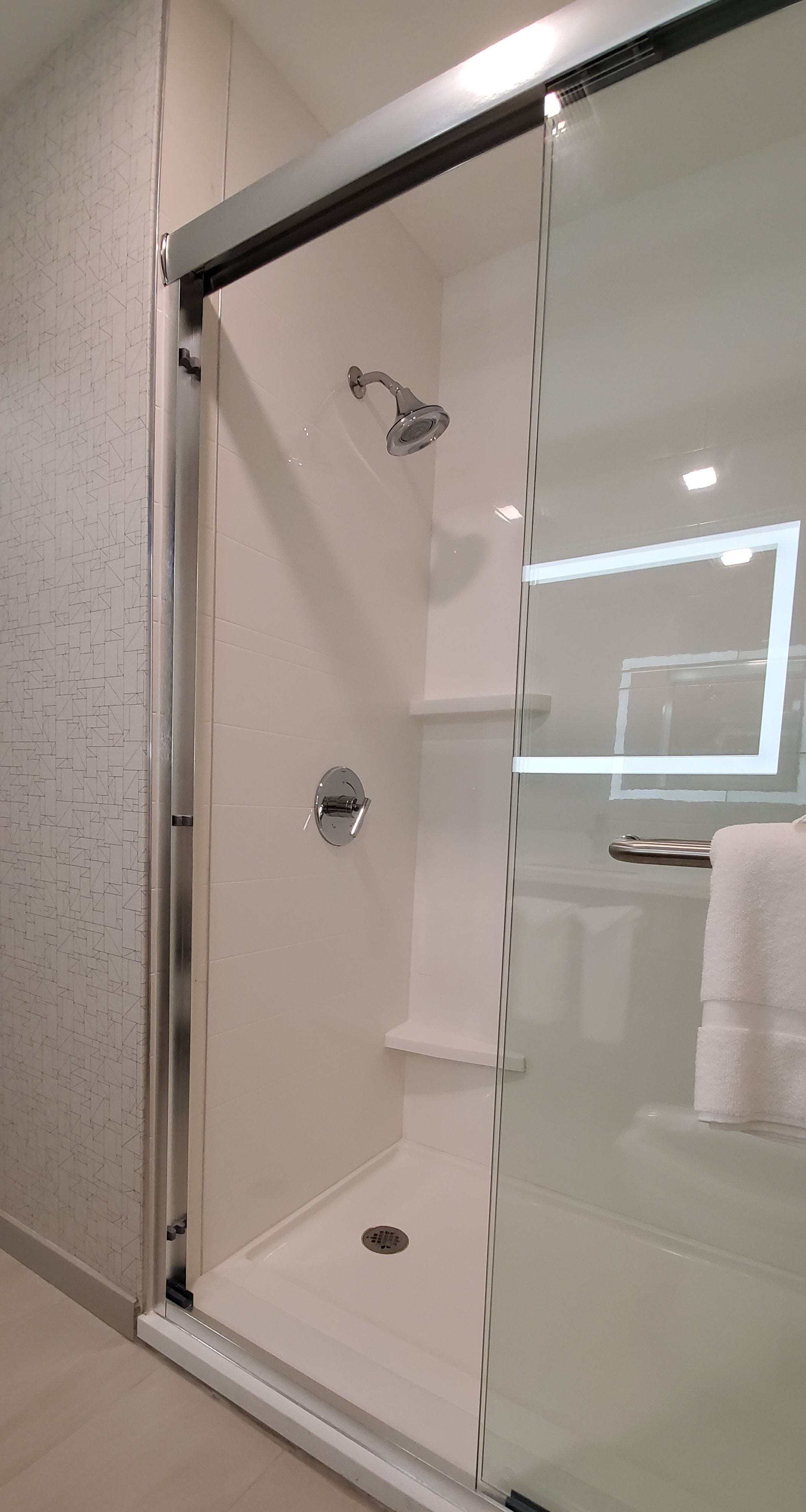 Une douche fermée par des parois de verre, dotée d’un pommeau de douche chromé et d’un mur recouvert de carreaux blancs.