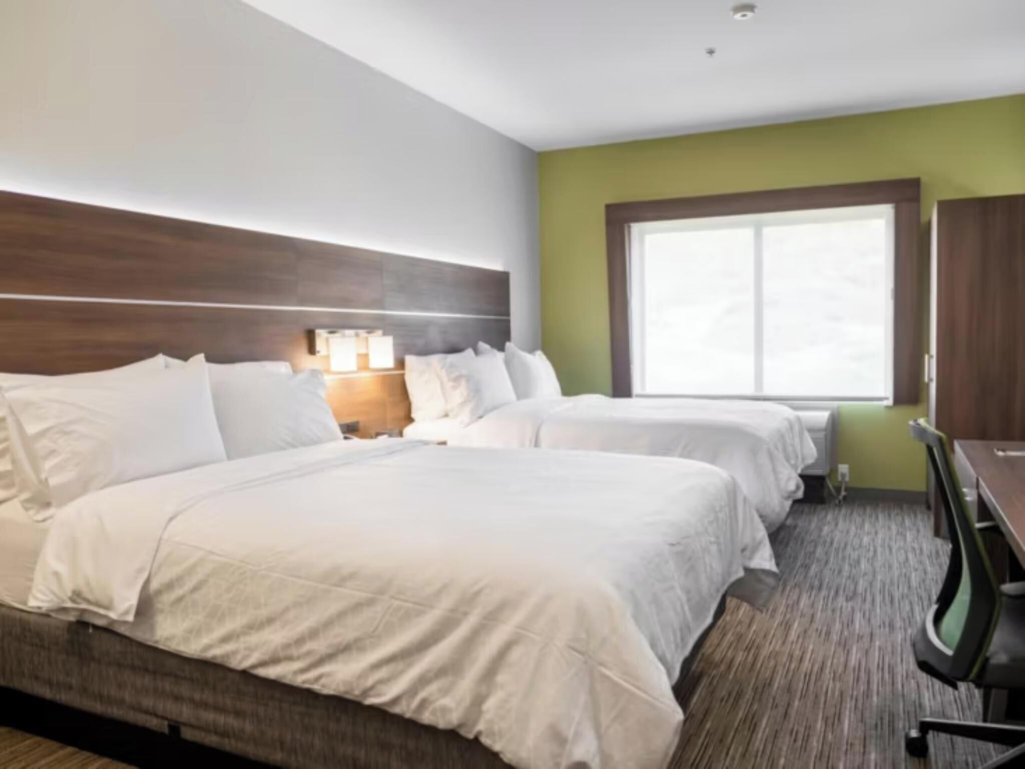 A hotel room with two beds, a nightstand, a desk, and a window.