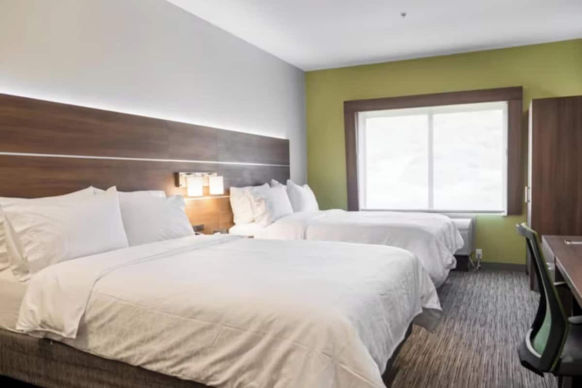 A hotel room with two beds, a nightstand, a desk, and a window.