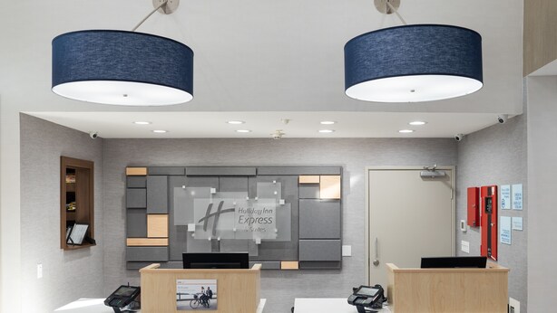 A modern hotel reception area with two reception desks, a large digital display, and a wall-mounted sign. - Holiday Inn Express & Suites Lake Forest by IHG (Lake Forest)
