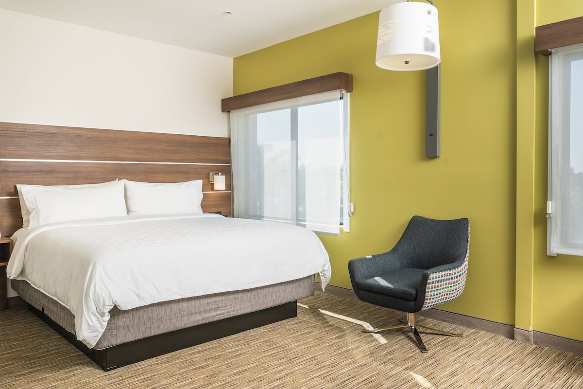 Habitación de hotel moderna con una cama grande, una silla, un ventanal y una lámpara fijada a la pared.