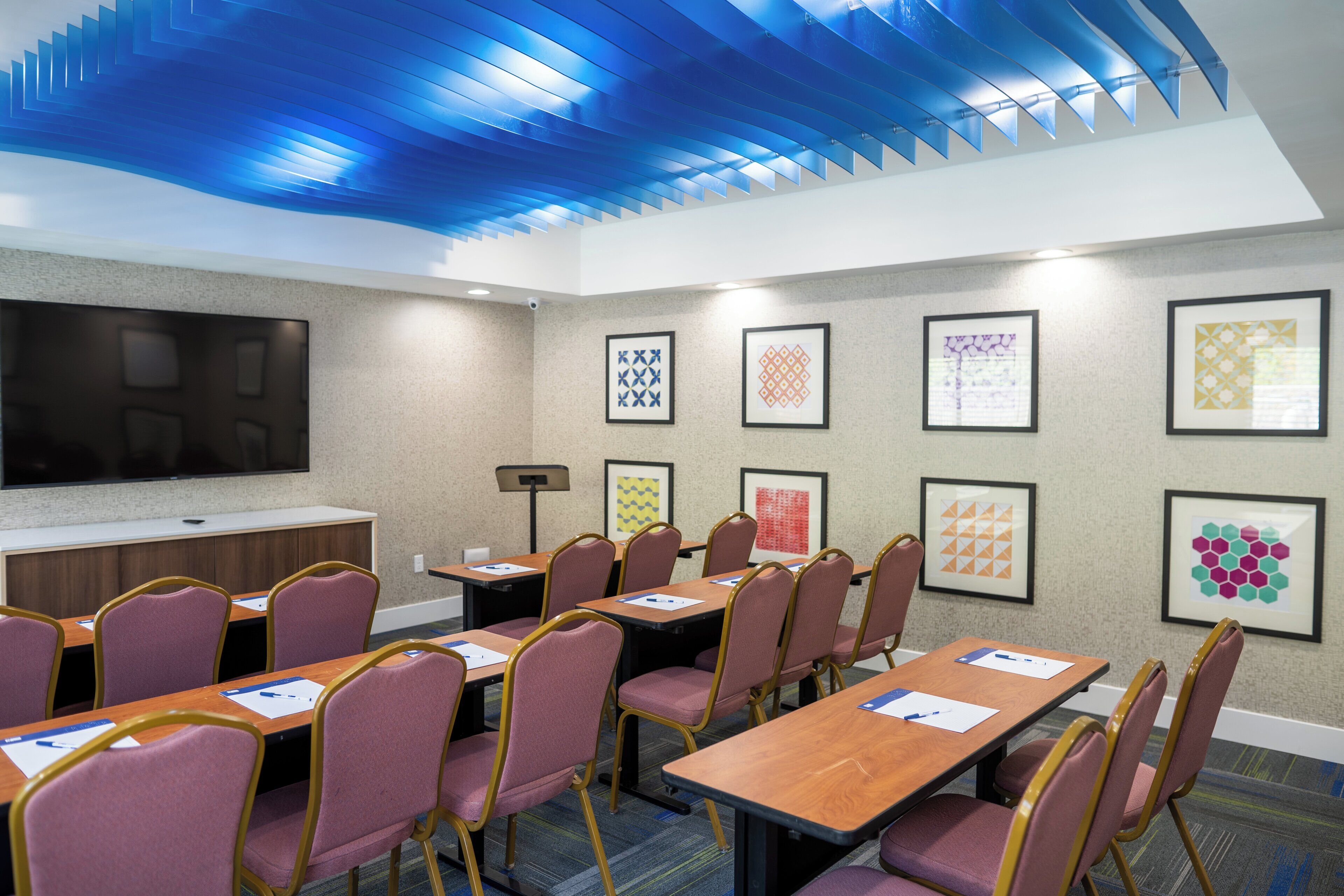 Un salón de conferencias con una mesa larga, sillas, un televisor de pantalla plana y obras de arte enmarcadas en las paredes.